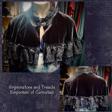 Dark velvet cloak with lace trim on a mannequin against a textured purple background.