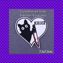 An embroidered patch of a cartoon black cat holding a knife with blood on a white heart background and the word "Killer"