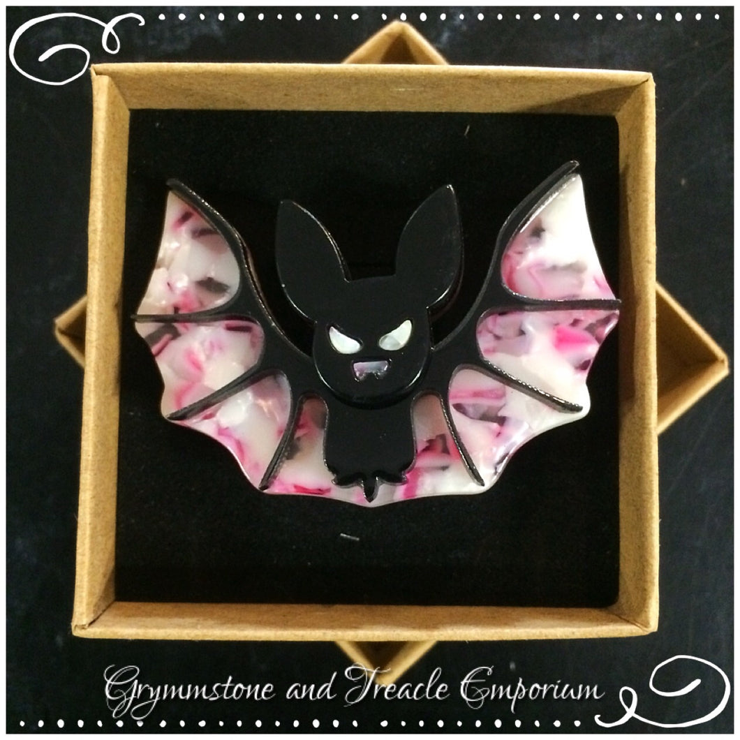 Celluloid brooch in the shape of an adorable bat with stretched wings, in pink, white and black